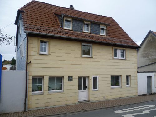 Ein Haus mit braunem Dach und weißen Fenstern, umgeben von einer grünen Landschaft.