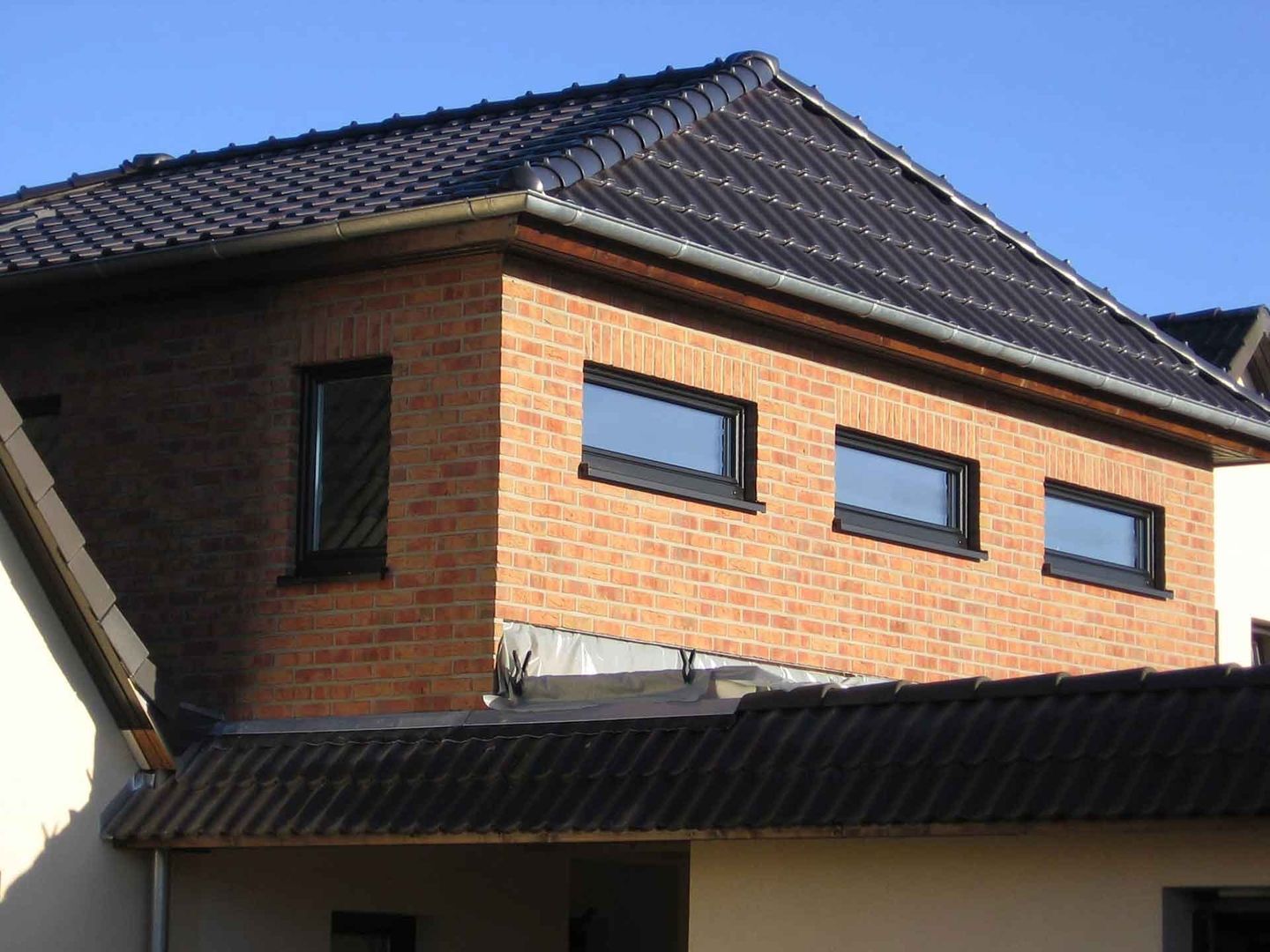 Maison avec un toit, entourée d'un jardin verdoyant et d'un ciel bleu clair.