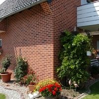 A charming house featuring a balcony, surrounded by a lush garden in the foreground.
