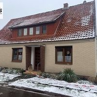 Ein Haus mit rotem Dach, umgeben von Schnee, der den Boden bedeckt und eine winterliche Atmosphäre schafft.