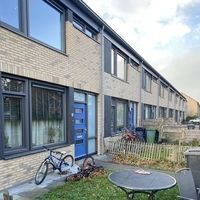 Ein Haus mit einem Fahrrad im Garten, umgeben von grüner Rasenfläche und blühenden Pflanzen.