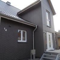 Ein graues Haus mit einem schlichten Design, umgeben von einer grünen Wiese und einem klaren blauen Himmel.