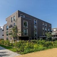 Modernes Wohngebäude mit einem Gehweg und Bäumen, umgeben von einer einladenden Landschaft.