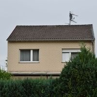 Ein helles Haus in der ferne was von Hecken und Bäumen umgeben ist.