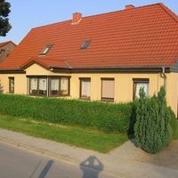 Ein Haus in einen Sandton mit orangenen Dach und einer Hecke davor.
