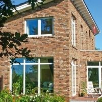 Ein Backsteinhaus mit einer Terrasse und einem Tisch, umgeben von einer einladenden Gartenlandschaft.