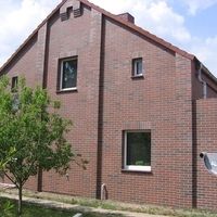 Une maison en brique avec un toit blanc, entourée d'une campagne verdoyante et d'un ciel clair.