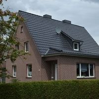Ein Haus mit einem Metall-Dach, das modern und langlebig wirkt, umgeben von einer grünen Landschaft.