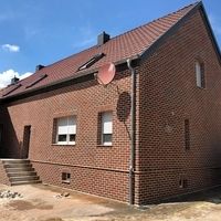 Une maison en brique avec un toit rouge, entourée d'une campagne verdoyante et d'un ciel clair.