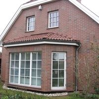 Ein Haus mit einem roten Dach, umgeben von einer grünen Landschaft und klarem Himmel.