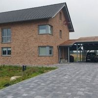 Ein Backsteinhaus mit einer Auffahrt und einem geparkten Auto im Vordergrund.