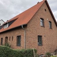 Ein Backsteinhaus mit rotem Dach und einem Fenster, umgeben von einer grünen Landschaft.