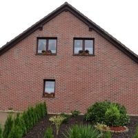 Une maison en brique avec une petite fenêtre, entourée d'un jardin bien entretenu.