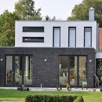 Modernes Haus mit einem gepflegten Garten und einer grünen Rasenfläche im Vordergrund.