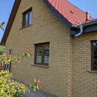 Ein Haus mit rotem Dach, umgeben von grüner Landschaft und klarem Himmel, strahlt Gemütlichkeit und Wärme aus.