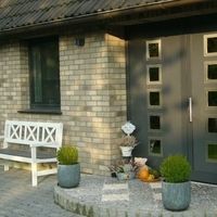 A quaint brick house featuring a bench in front and a welcoming door, surrounded by a serene outdoor setting.