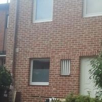 Une voiture rouge est garée devant une maison en briques qui dégage une atmosphère charmante et accueillante.