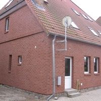 Rotes Backsteinhaus mit einer Satellitenschüssel auf dem Dach, umgeben von einem grünen Garten.
